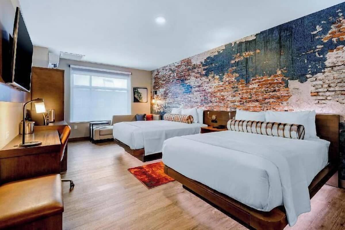 Ein Hotelzimmer mit zwei Betten, einem Schreibtisch, einem Fernseher und einer großen Wandmalerei aus Ziegelsteinen.