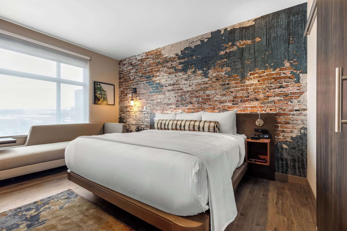Ein modernes Schlafzimmer mit einem großen Bett, einer Couch, einer Ziegelwand und Blick auf die Stadt.