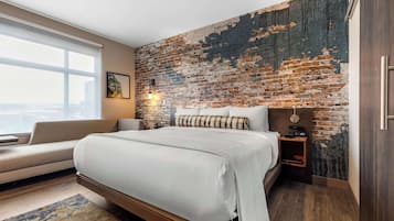 A modern bedroom with a large bed, a sofa, a brick wall, and a city view.
