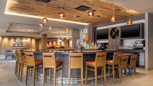Een moderne bar met een centraal gelegen bar eiland, barstoelen en een grote flatscreen televisie.