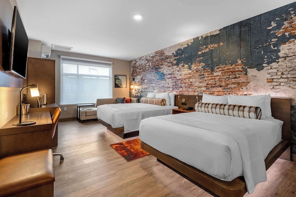 Une chambre d’hôtel avec deux lits, un bureau, une télévision et un mur en briques.