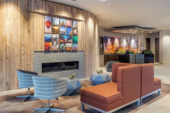 A modern lobby with a wooden wall, a fireplace, and a seating area with a sofa and chairs.