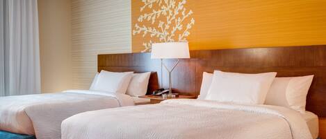 A hotel room with two beds, a wooden headboard, a nightstand with a lamp, and a decorative wall panel.