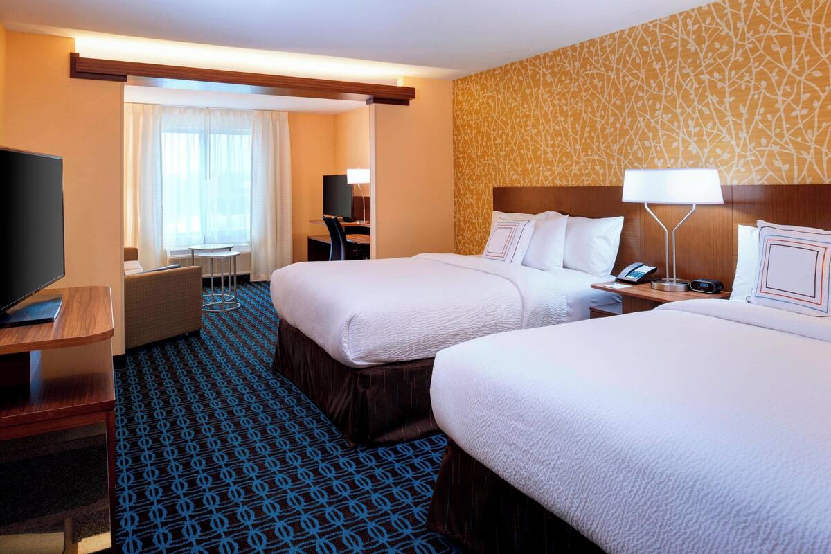 A hotel room with two beds, a desk, a TV, and a chair.