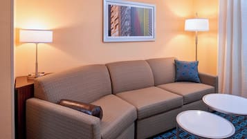 A hotel room with a sofa, two side tables, a framed picture on the wall, and a patterned rug.