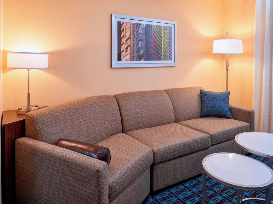 A hotel room with a sofa, two side tables, a framed picture on the wall, and a patterned rug.