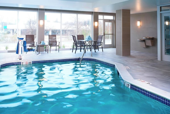 Una piscina con indicador de profundidad de 3.6 metros, rodeada de sillas y una mesa, con ventanas amplias que ofrecen vistas al exterior.