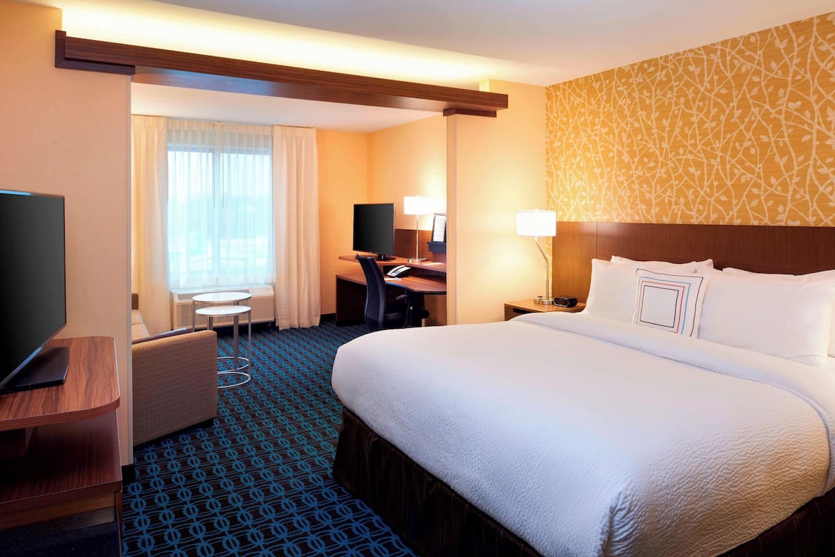 A hotel room with a large bed, a desk with a computer, a TV, and a seating area with a chair and table.