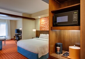 Une chambre d’hôtel équipée d’un lit, d’un bureau avec un ordinateur, d’une télévision, d’un four à micro-ondes et d’une machine à café.