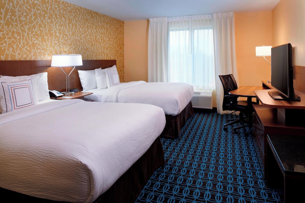 A hotel room with two beds, a desk with a television, a chair, and a patterned carpet.