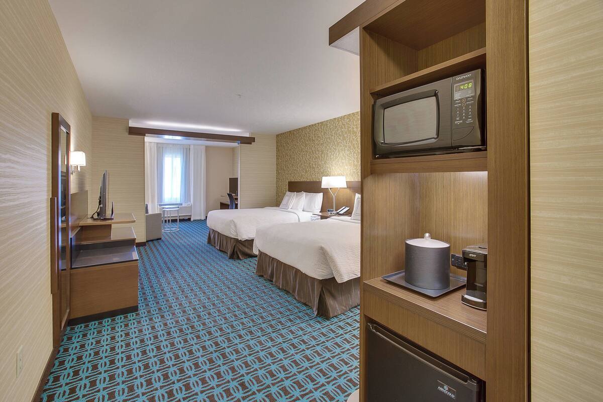 Ein Hotelzimmer mit zwei Betten, einer Mikrowelle, einer Kaffeemaschine und einem Schreibtisch mit Lampe.