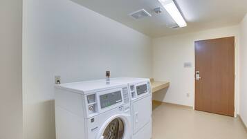 A laundry room with a stacked washer and dryer, a wooden door, and a small shelf.