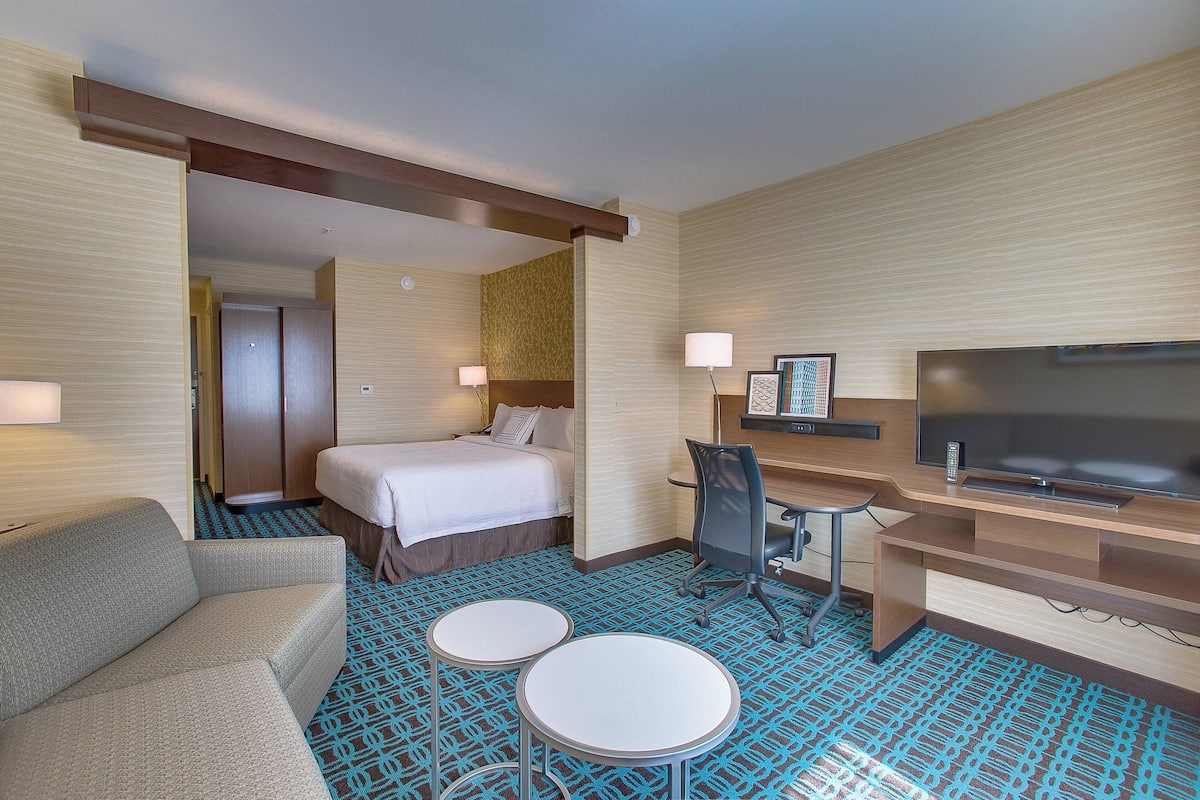 Ein Hotelzimmer mit einem Bett, einem Schreibtisch mit Fernseher, einer Couch und zwei kleinen Tischen.