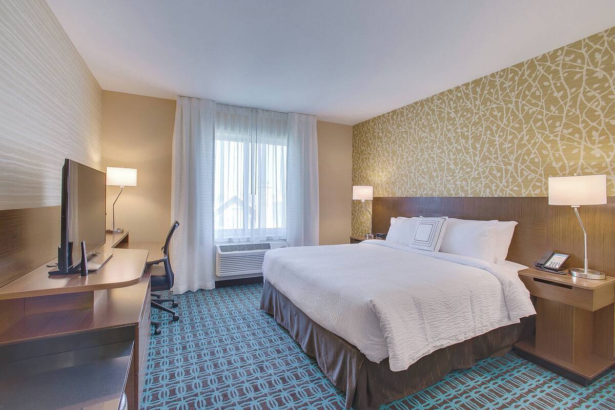 Ein Hotelzimmer mit Bett, Nachttischen, Schreibtisch, Sessel und einem Teppich mit Muster.