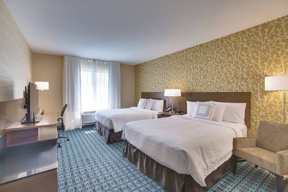 Ein Hotelzimmer mit zwei Betten, einem Schreibtisch, einem Stuhl und einem Fernseher.