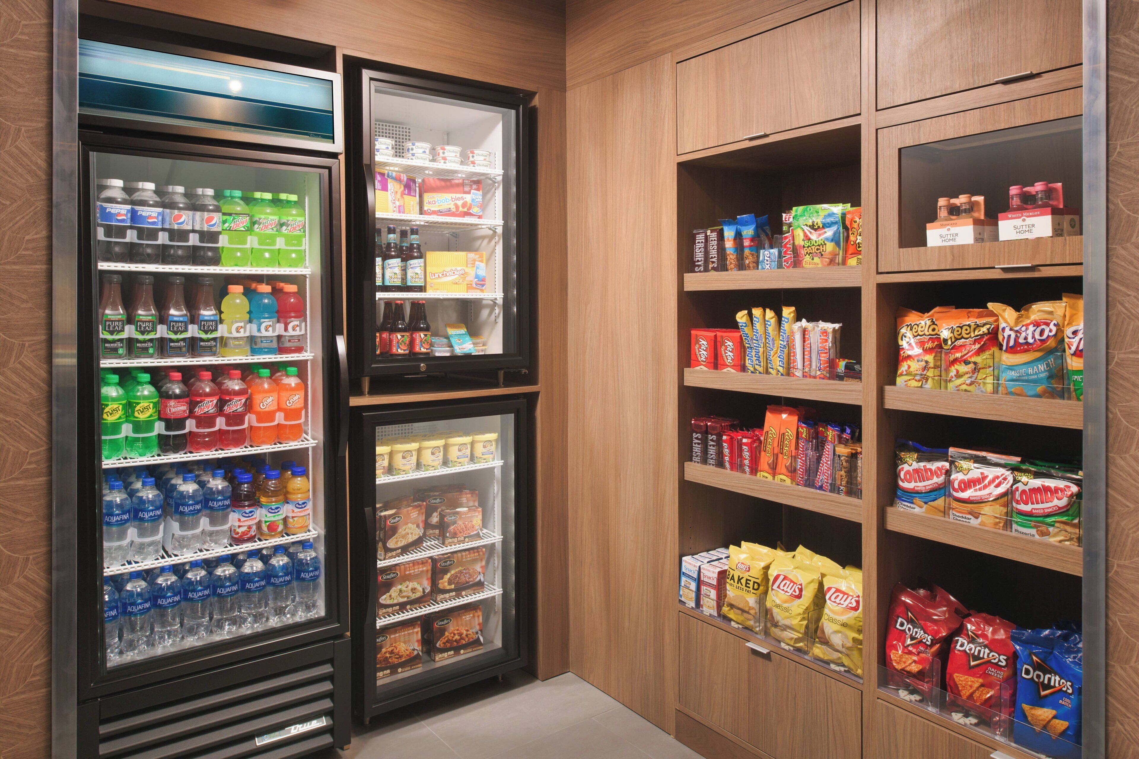 Ein gekühlter Getränkeautomat, gefüllt mit verschiedenen Getränken, und ein Regal mit Snacks wie Chips und anderen Leckereien.