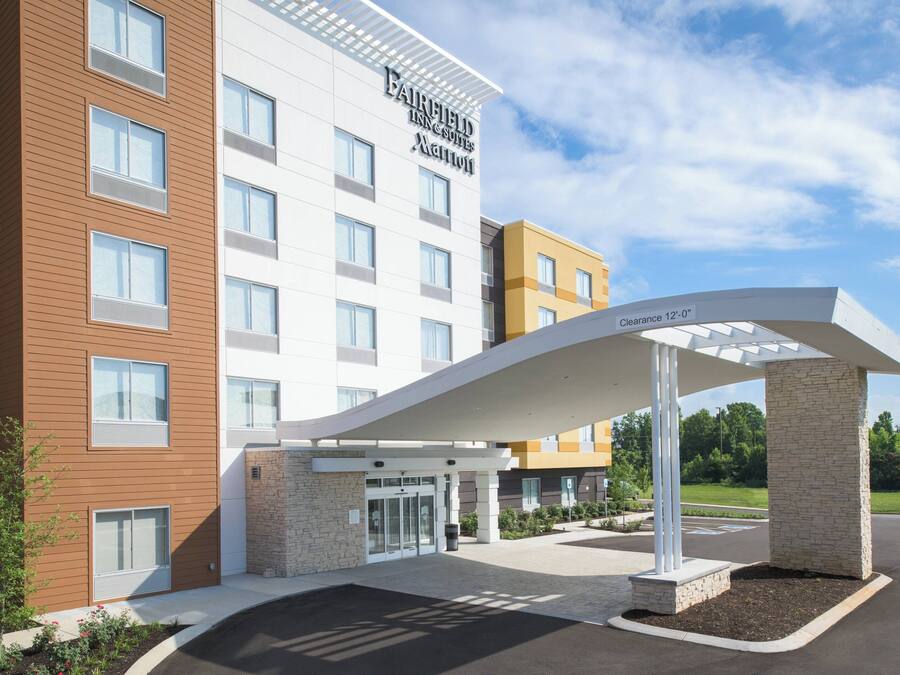A Fairfield Inn & Suites hotel with a modern entrance, clear signage, and a landscaped area with a covered walkway.