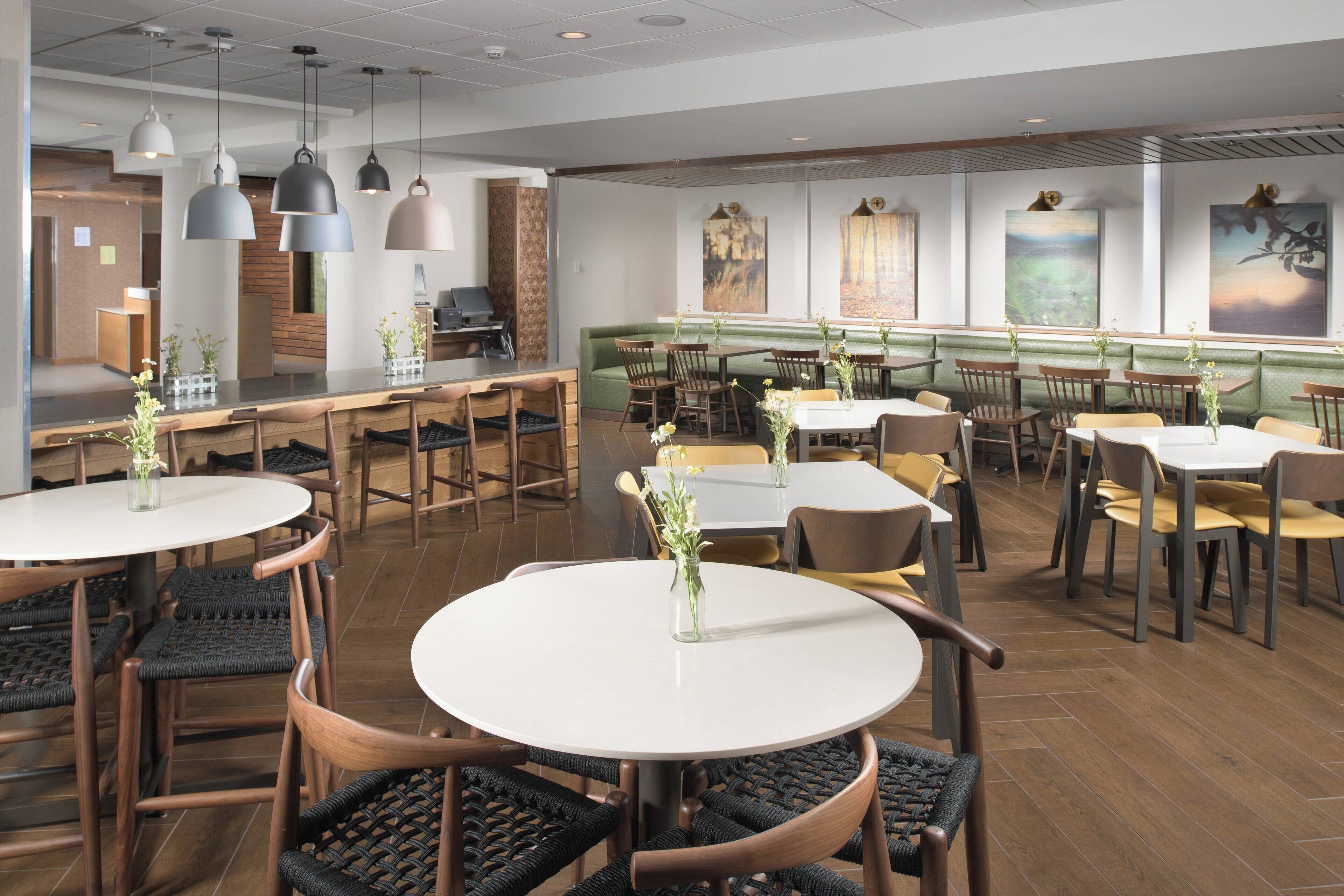 A restaurant with round tables, chairs, and hanging pendant lights.