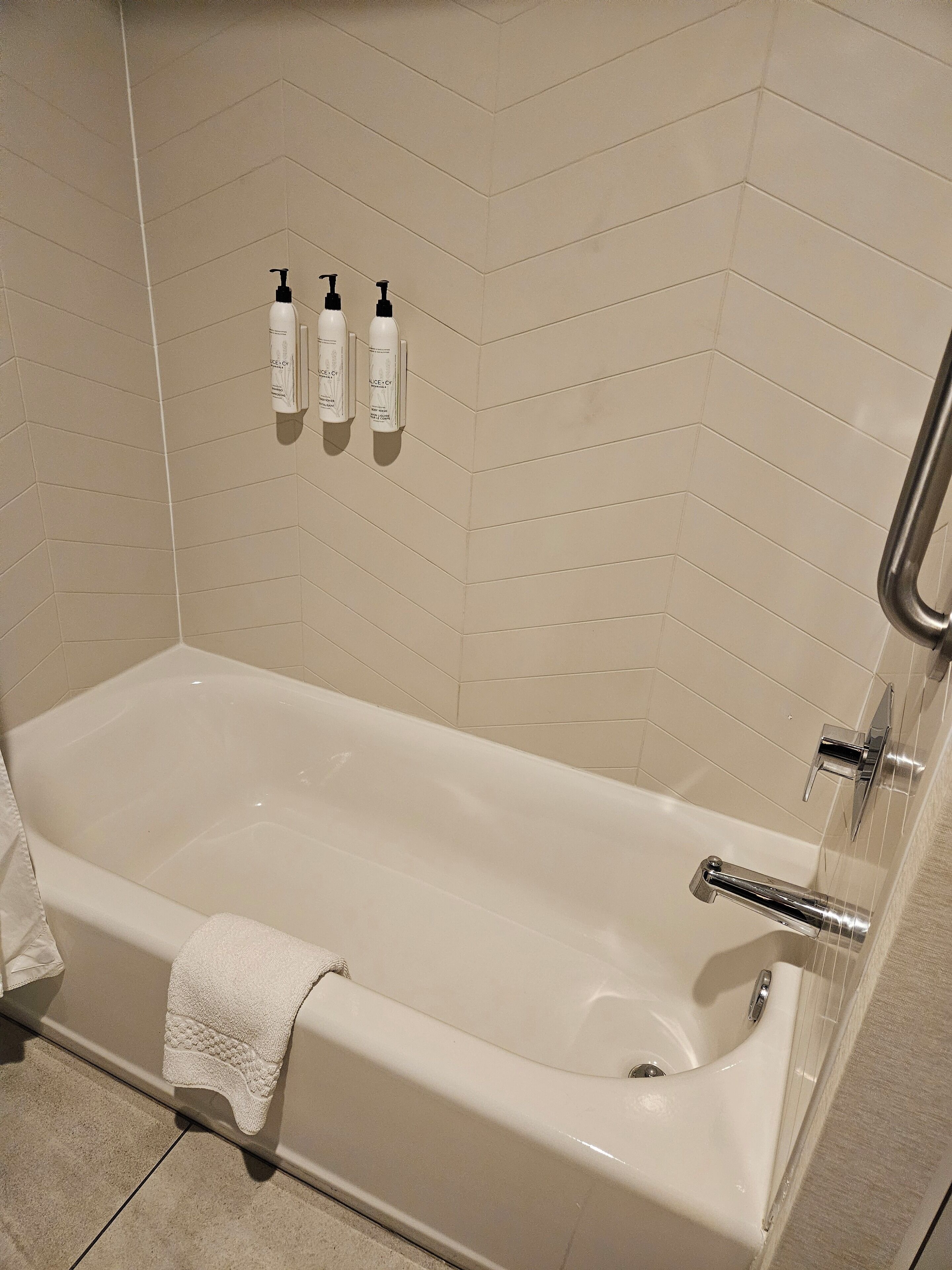 A modern bathroom with a freestanding bathtub, a towel, and three bottles of shampoo on the wall.