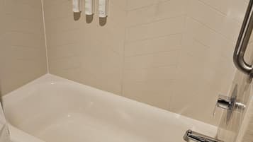 A modern bathroom with a freestanding bathtub, a towel, and three bottles of shampoo on the wall.
