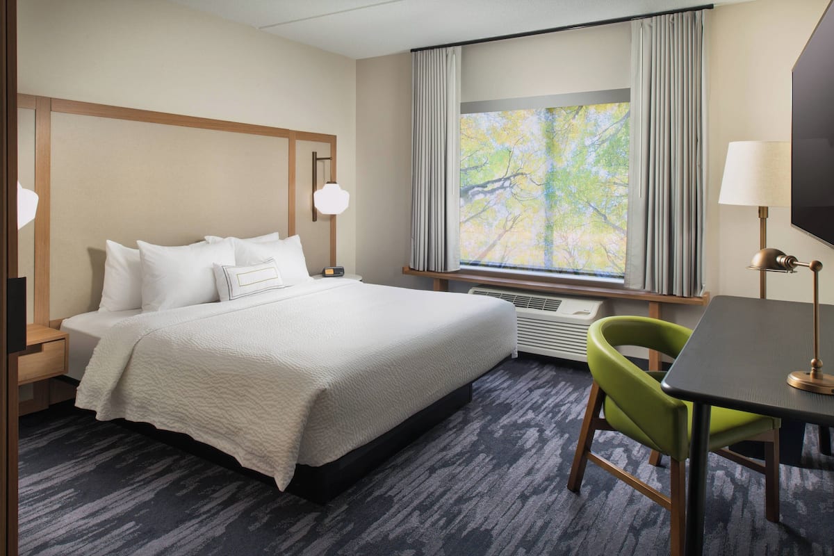 A hotel room with a bed, a desk, a chair, a TV, and a window with curtains.