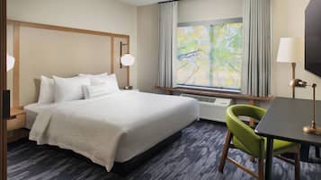 A hotel room with a bed, a desk, a chair, a TV, and a window with curtains.
