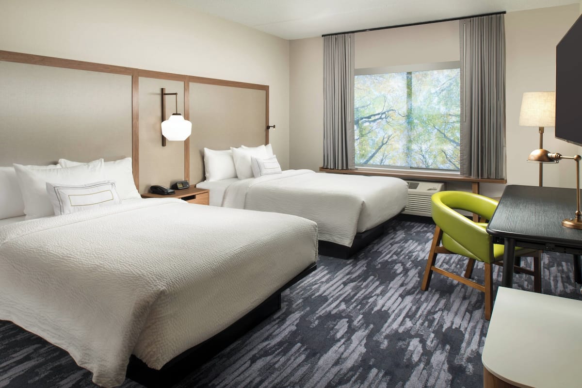A hotel room with two beds, a desk, a chair, and a large window with curtains.