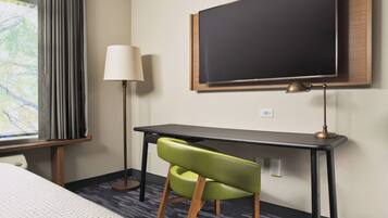 Habitación de hotel con cama, escritorio, silla, televisor y lámpara.