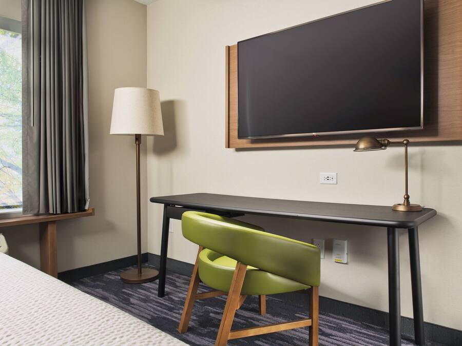 Habitación de hotel con cama, escritorio, silla, televisor y lámpara.