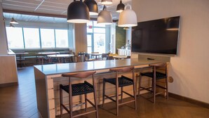 A modern bar area with a long counter, bar stools, pendant lighting, and a large flat-screen TV.