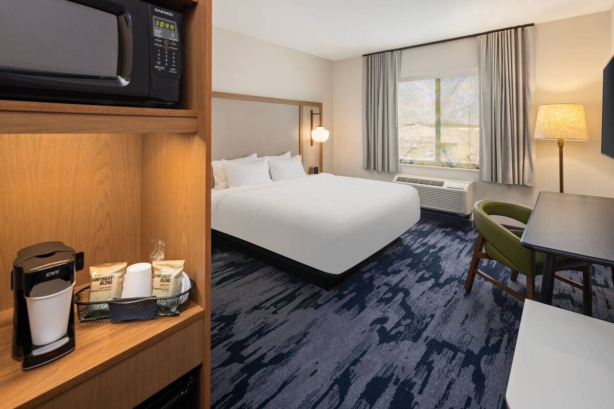 A hotel room with a bed, a desk, a chair, a coffee maker, and a tray with coffee pods.