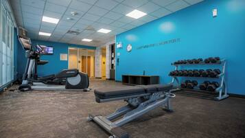 A gym with cardio equipment, dumbbells, and a motivational quote on the wall.
