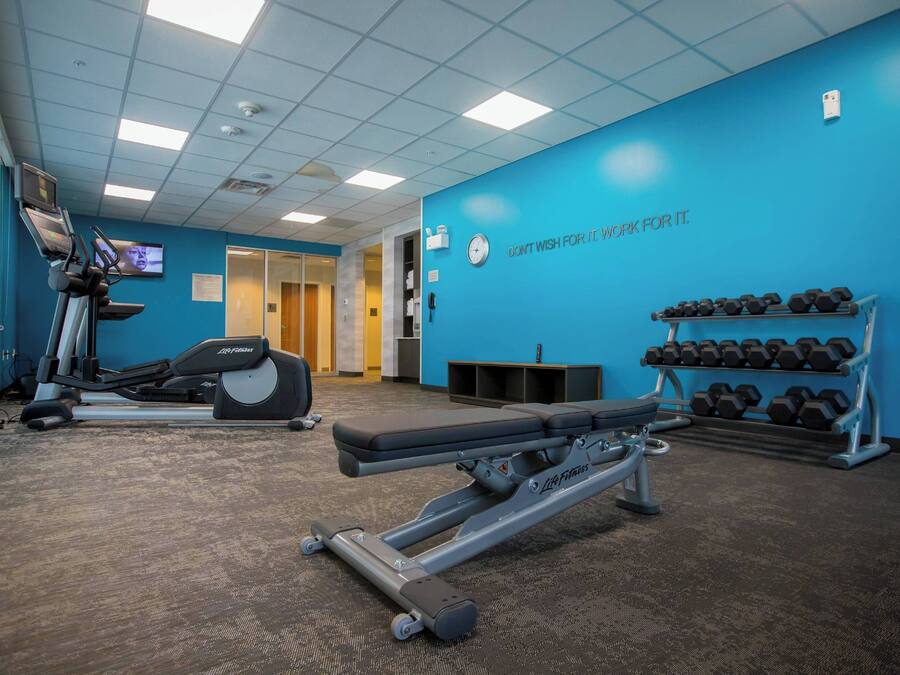 A gym with cardio equipment, dumbbells, and a motivational quote on the wall.
