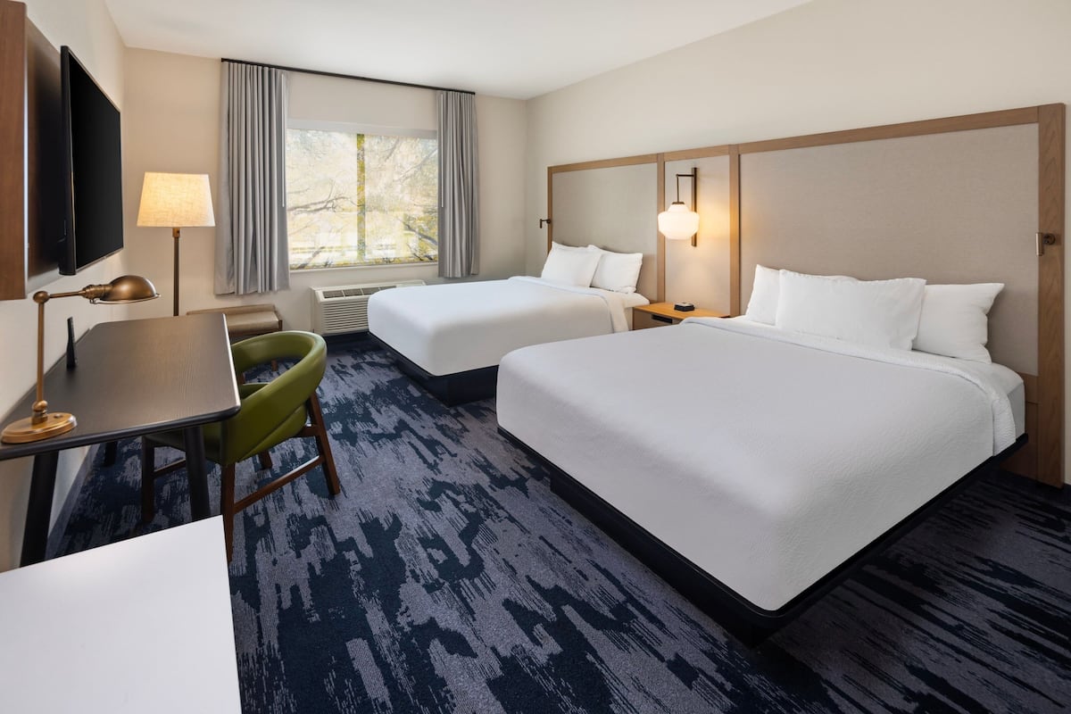 A hotel room with two beds, a desk, a chair, a TV, and a window with curtains.