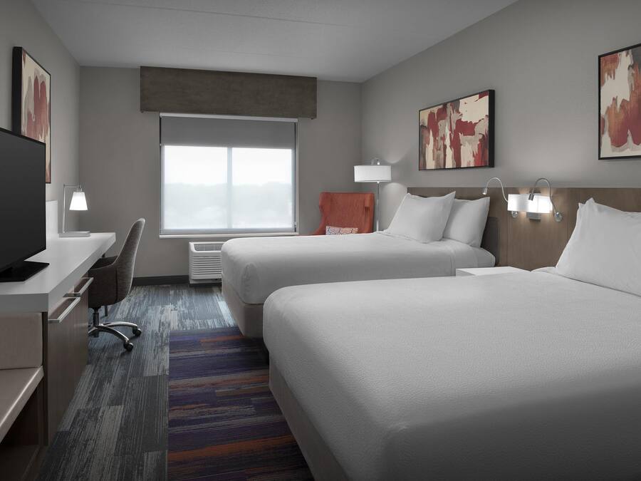 A hotel room with two beds, a desk, a TV, and a large window.