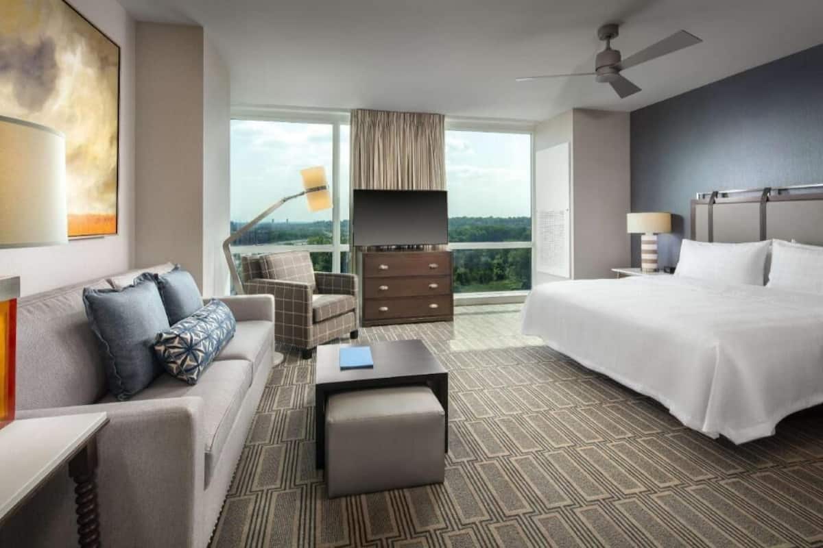 Ein Hotelzimmer mit Bett, Sofa, Sessel, Kommode, Schreibtisch und einem großen Fenster mit Blick.