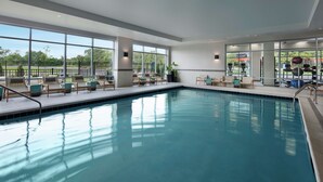 An indoor swimming pool with clear glass walls, lounge chairs, and exercise equipment. - Homewood Suites by Hilton Teaneck Glenpointe (Teaneck)