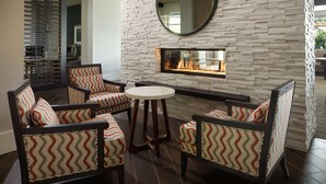 A modern lounge area with a fireplace, patterned chairs, and a round mirror. - Homewood Suites by Hilton Teaneck Glenpointe (Teaneck)
