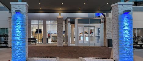 A hotel entrance with a modern design, featuring a brick facade and illuminated pillars.