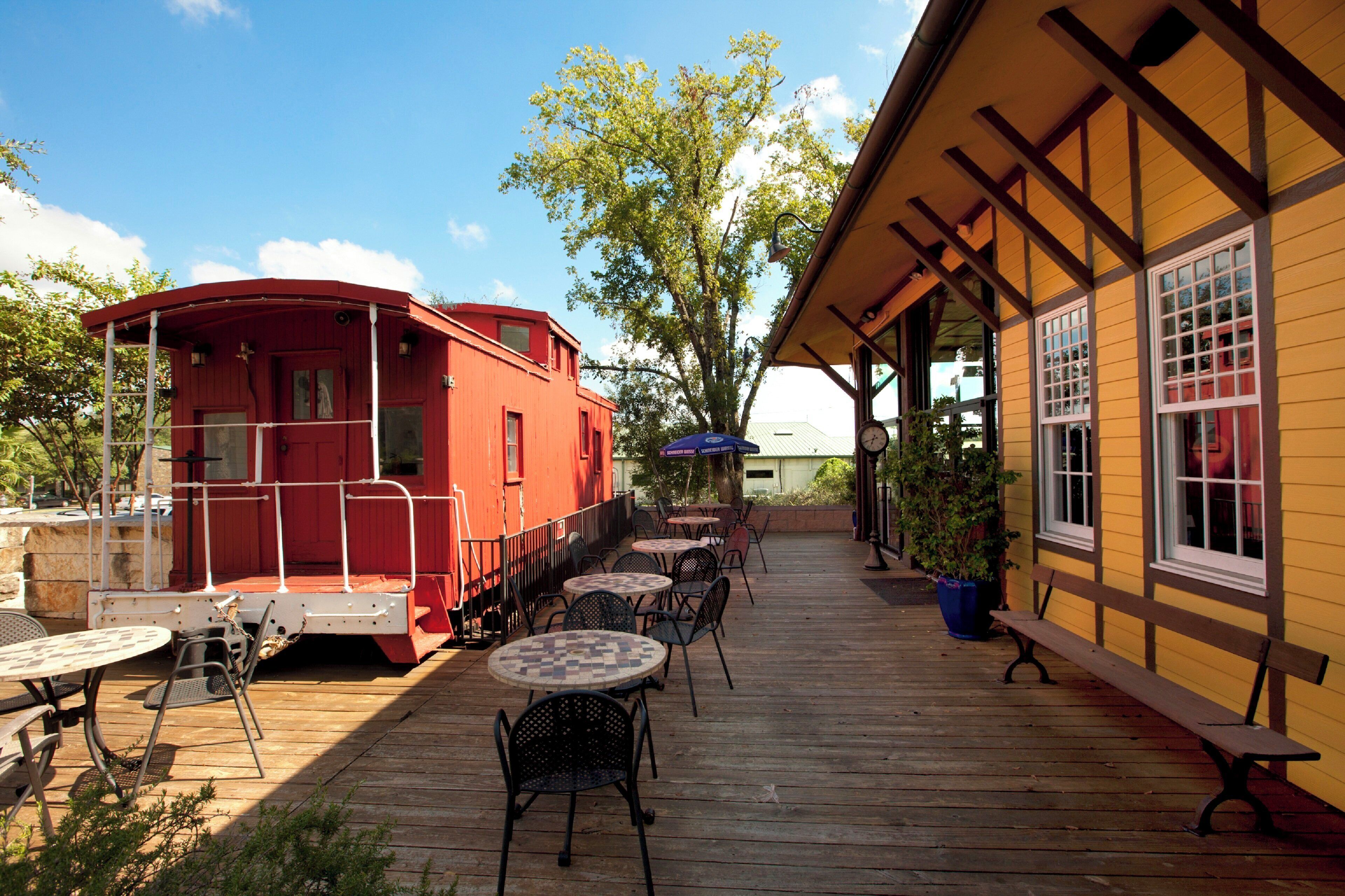 A wooden deck with outdoor seating, a red boat-shaped building, and a yellow building with windows.