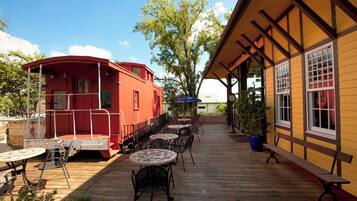 A wooden deck with outdoor seating, a red boat-shaped building, and a yellow building with windows.