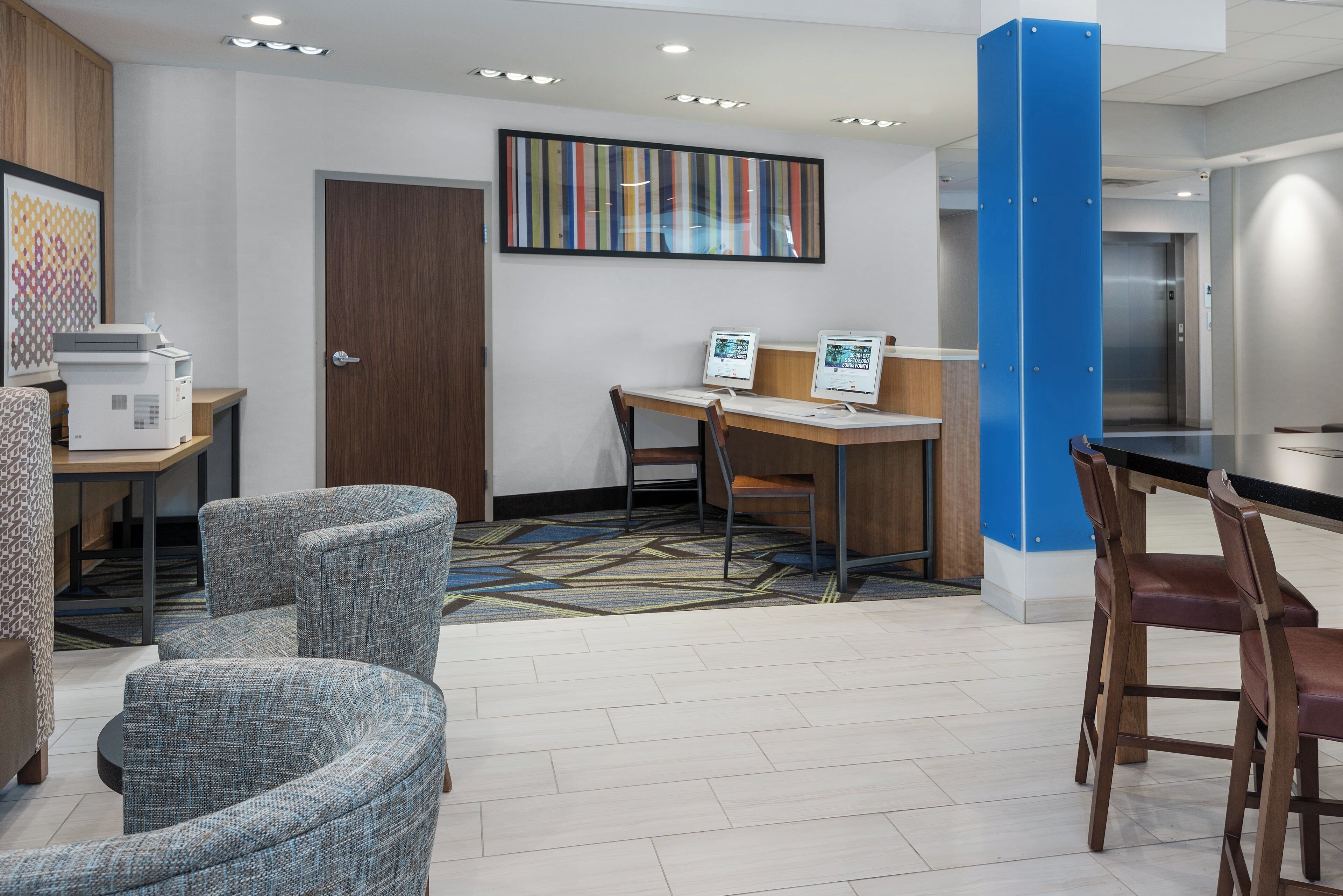 Un hall de hotel con mostrador de recepción, zona de estar y un pilar azul grande.