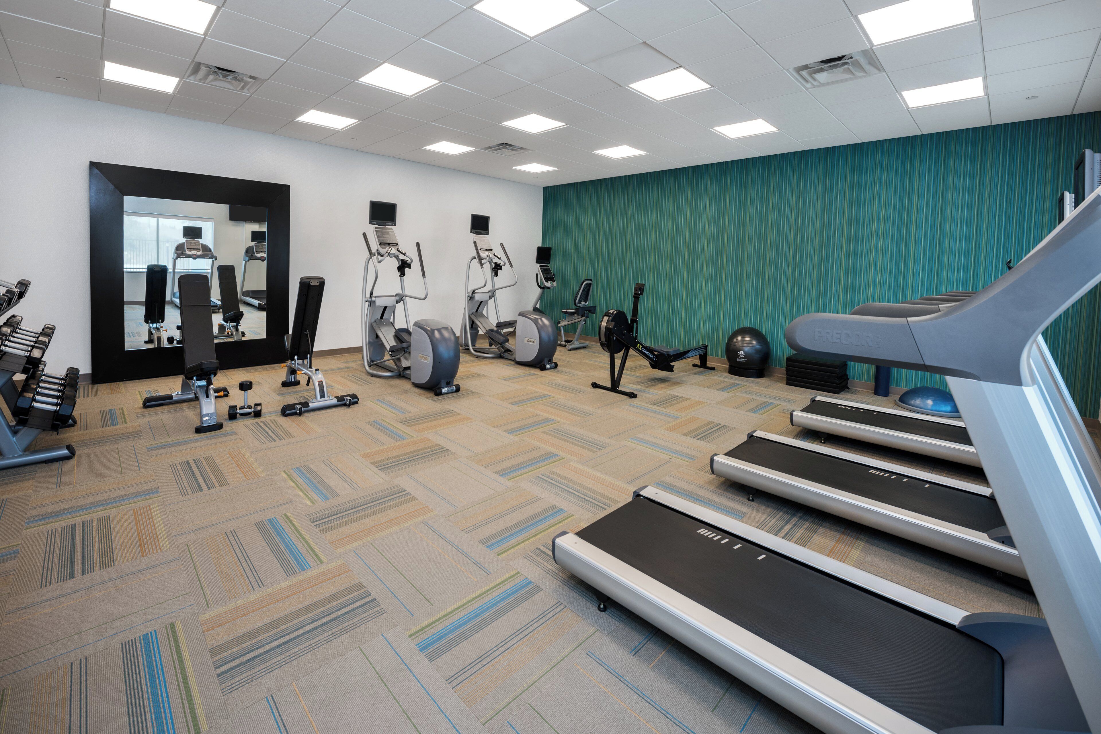 Un gimnasio con cintas de correr, elípticas y pesas libres.