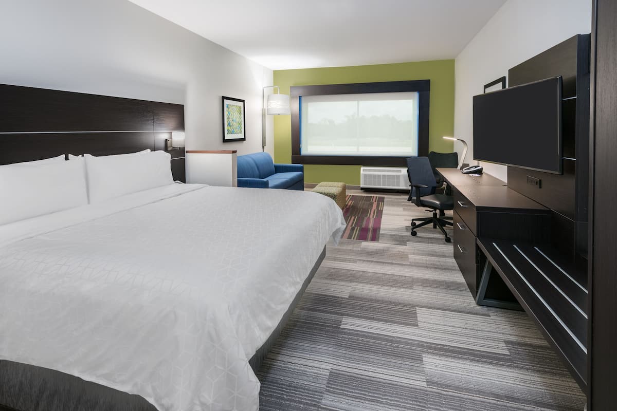 A hotel room with a large bed, a desk with a computer, a TV, and a window with a view of trees.