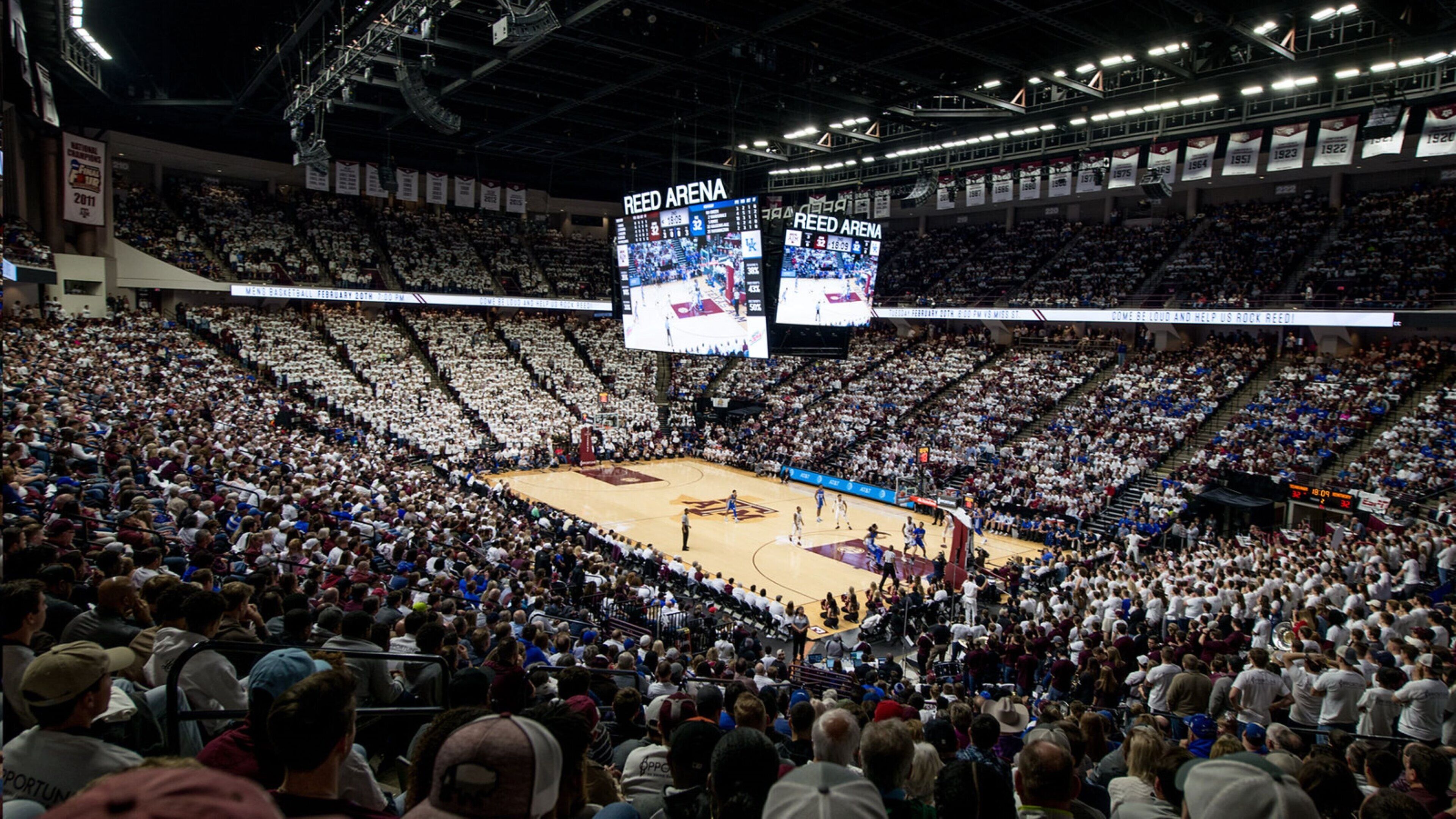 Un vaste stade intérieur doté de nombreuses rangées de sièges, d’un terrain de basket-ball et de grands écrans numériques.