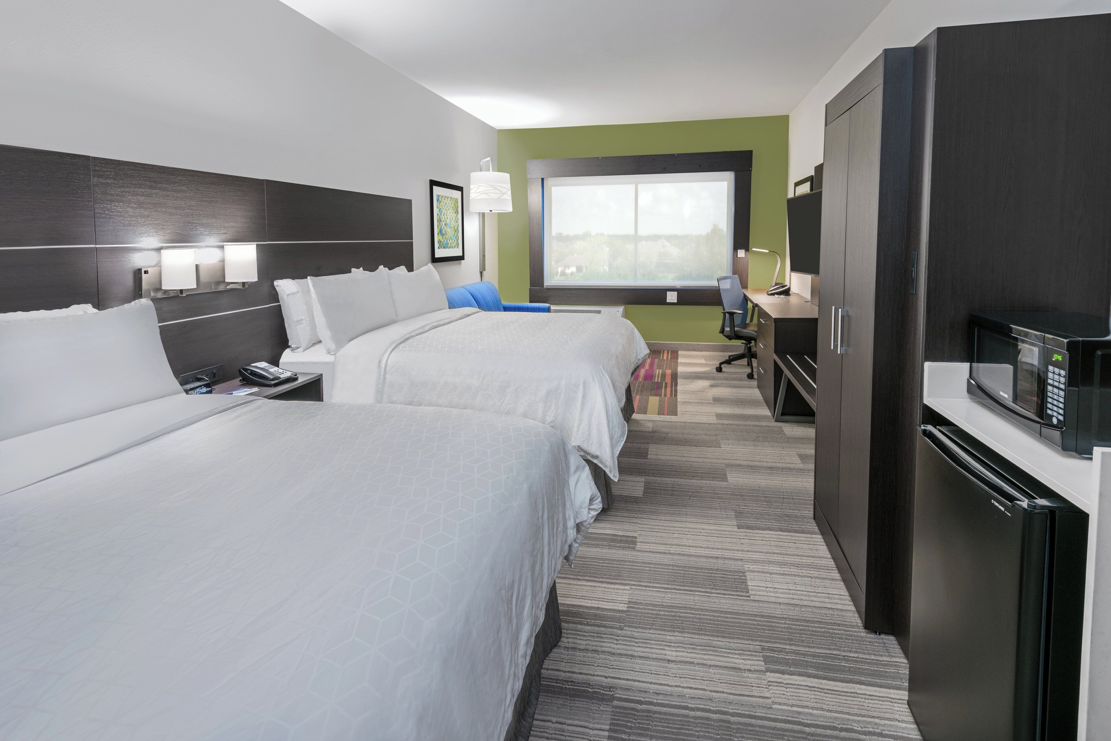 Une chambre d’hôtel avec deux lits, un bureau, une chaise, un four à micro-ondes et une grande fenêtre.