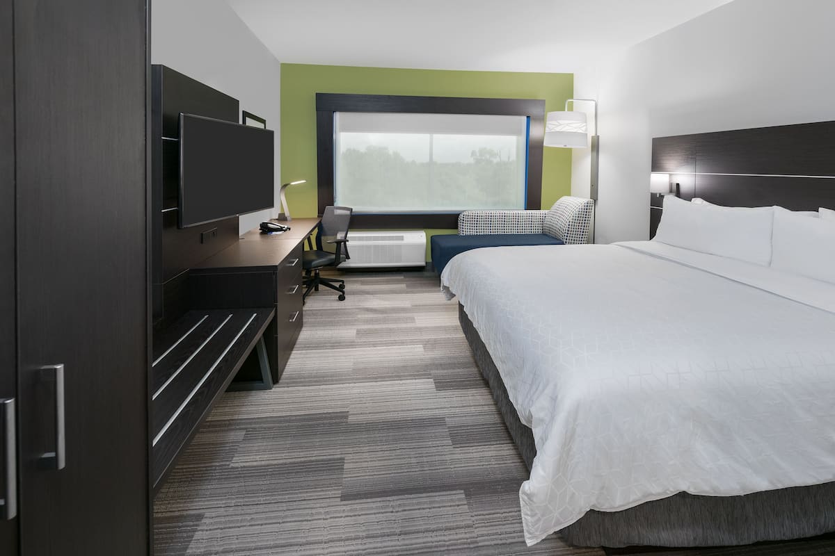 A hotel room with a bed, a desk with a chair, a television, and a window.