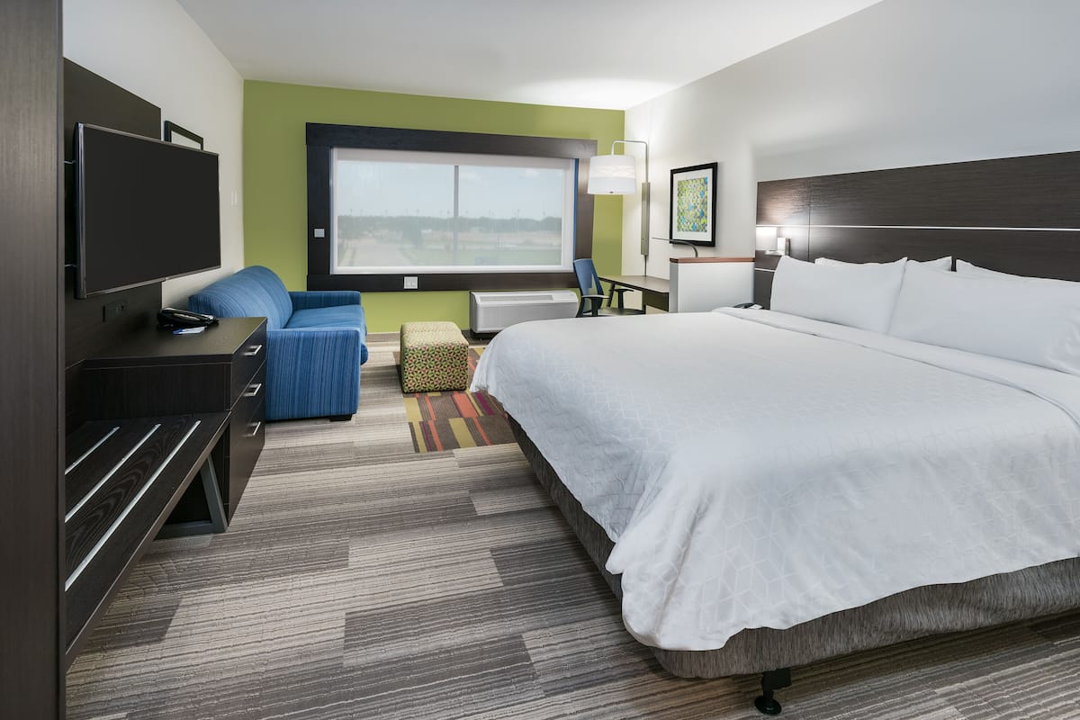 A hotel room with a large bed, a TV, a desk, a chair, and a window with a view.