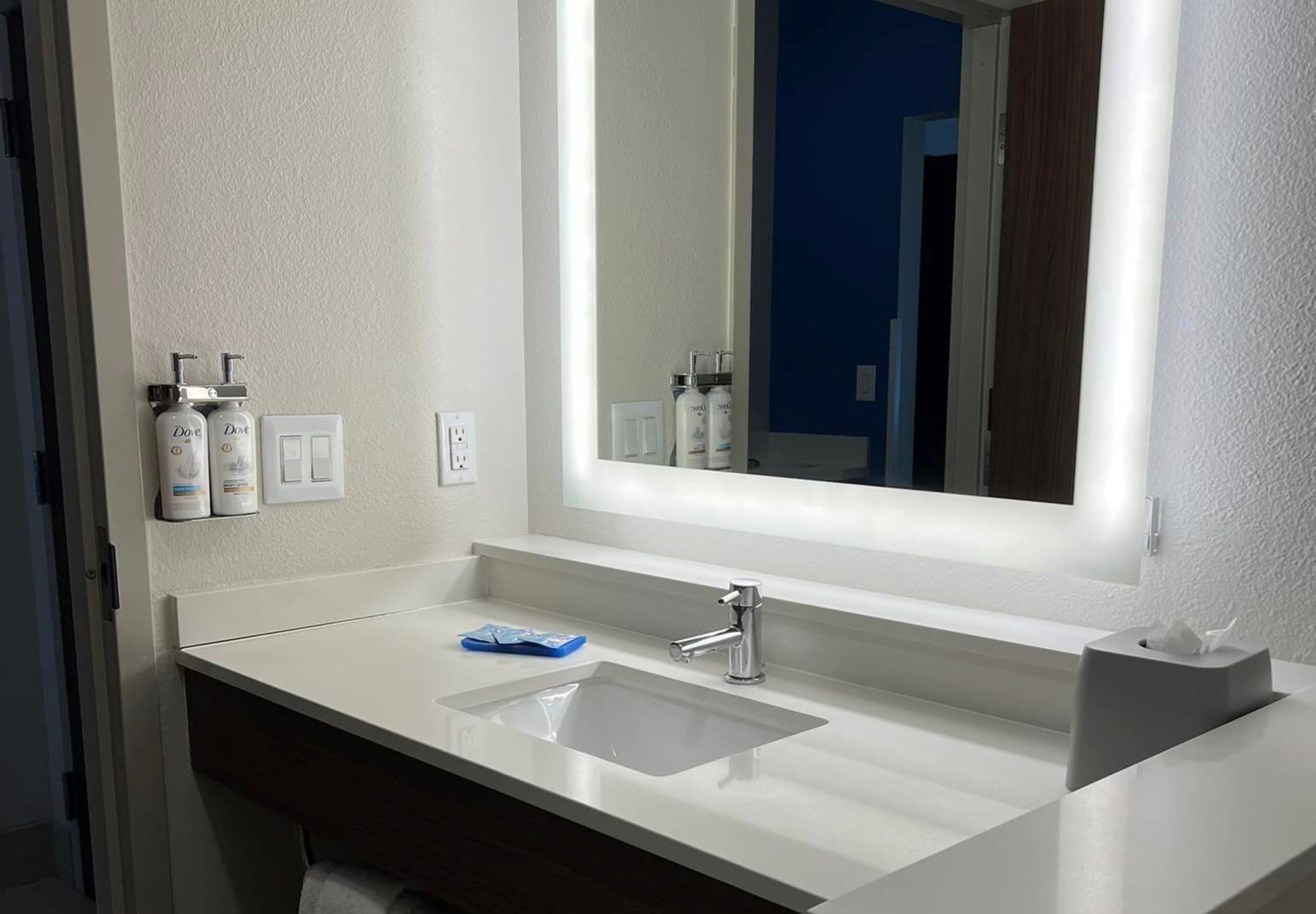 Un baño moderno con un lavabo blanco, un espejo grande y artículos de tocador en la pared.