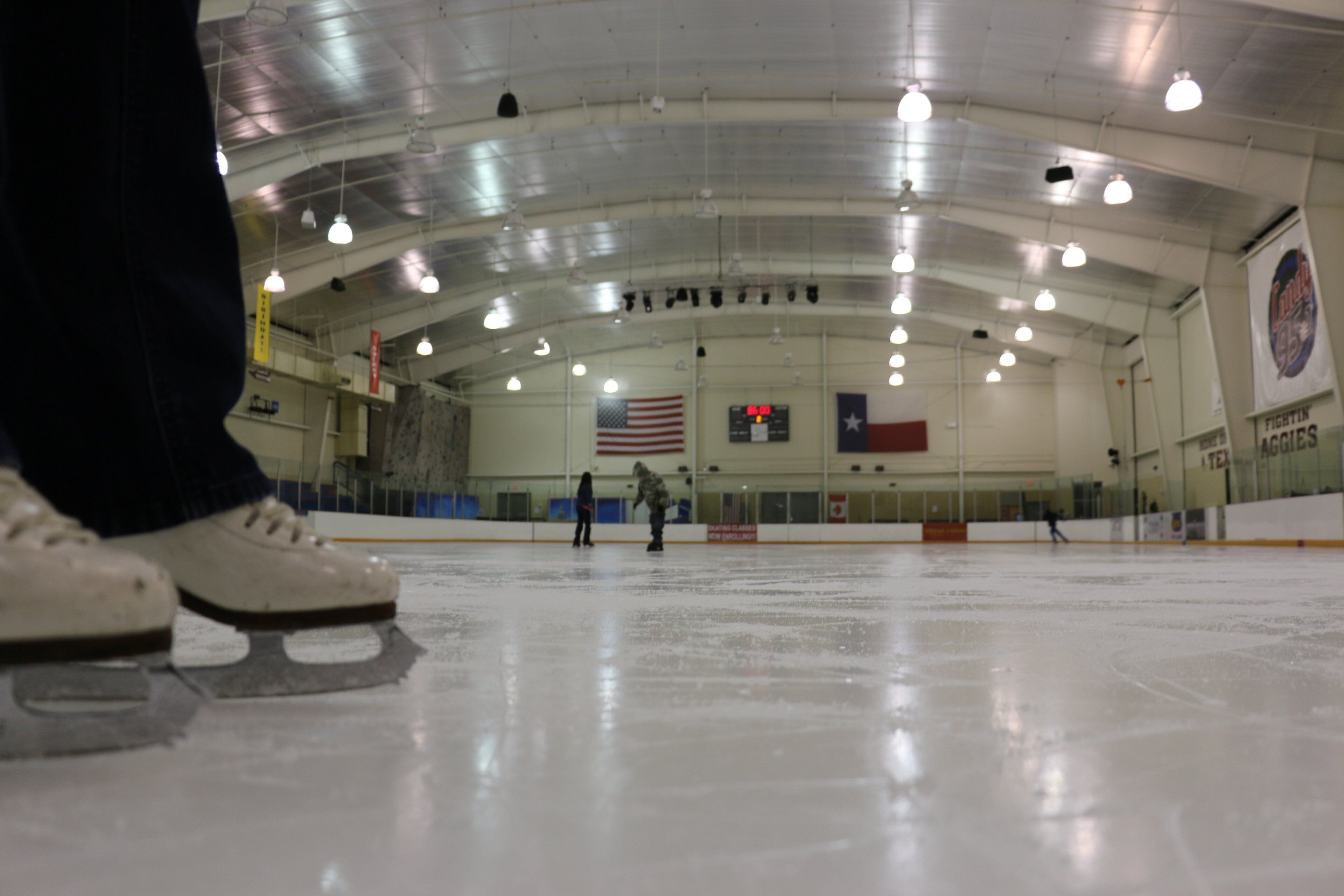 An indoor ice rink with overhead lighting, a scoreboard, and an American flag.